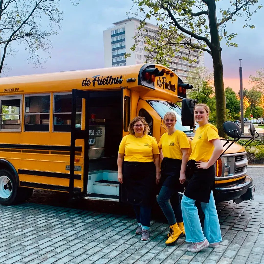 Het team van De Frietbus bij de gele schoolbus, te huur via Feestkarhuren.nl