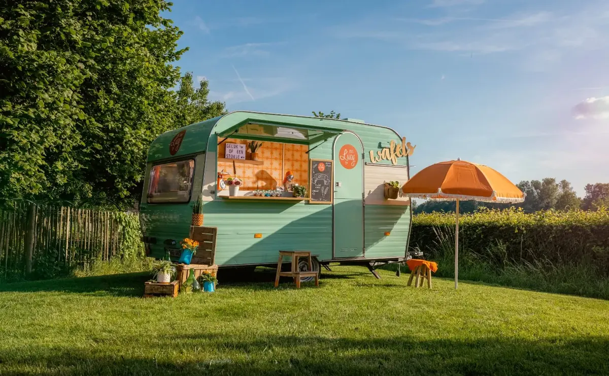 De caravan van Ons Lucy met parasol in het gras, te huur via Feestkarhuren.nl