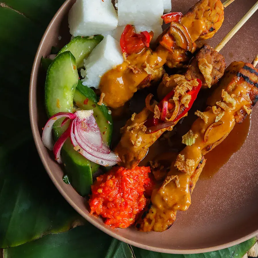 Een bord saté met komkommer en sambal