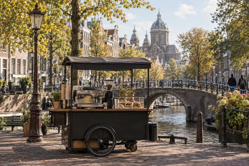 Koffiekar aan een gracht in Amsterdam met een stenen brug en de Sint-Nicolaasbasiliek